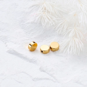 Macro view of three polished 14K gold-plated flat round spacer beads on stone