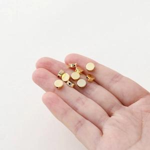 Macro detail of gold plated flat round spacer beads held in palm for size reference