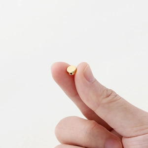 Close-up of a 14K gold-plated flat round spacer bead held between fingers for sizing