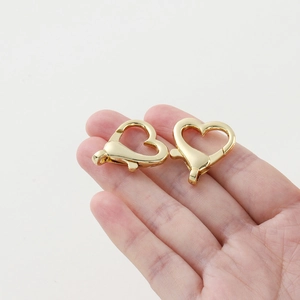Due moschettoni a forma di cuore color oro mostrati sulla mano per accessori fai-da-te