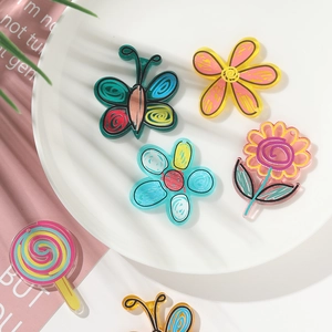 Flat lay of colorful acrylic flower and butterfly DIY charms on a white ceramic tray