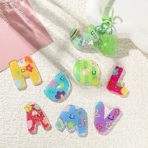 Pendentifs alphabet en acrylique coloré aux motifs mignons sur fond en peluche blanche