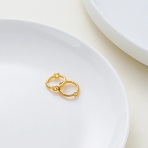 Primer plano de aretes de aro dorados trenzados con detalles florales de dos agujeros