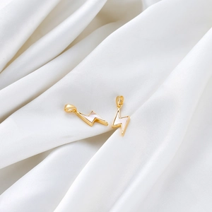 Close-up of gold lightning bolt charms with white mother of pearl on white silk fabric