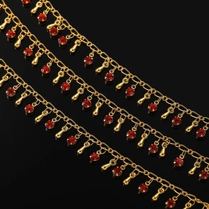 Détail d'une chaîne dorée ornée de cristaux rouges et de pendentifs goutte d'or