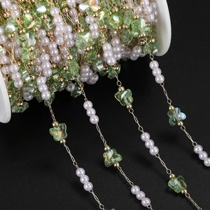 Detail of DIY jewelry chain with white pearls and green butterfly beads on a spool