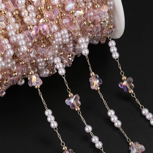 Macro shot of pink crystal butterfly and pearl copper chain on a white spool