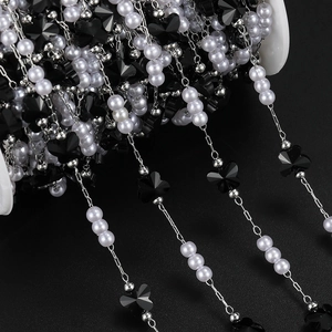 Macro detail of DIY jewelry chain with black butterfly beads and white pearls on a spool