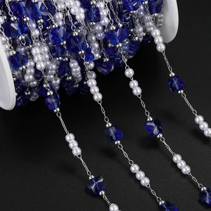 Detail of DIY jewelry chain with white faux pearls and blue butterfly beads on a spool