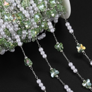 Macro detail of light green butterfly glass beads and white pearls on silver DIY chain