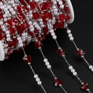 Detailed view of DIY bead chain with red butterfly charms and white pearls on a silver spool