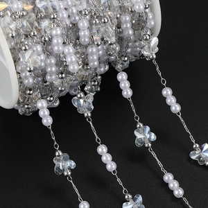 Detail of DIY jewelry chain with white pearls and butterfly charms on a spool