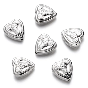 Detalle de abalorios de corazón plateado con relieve floral para joyería artesanal