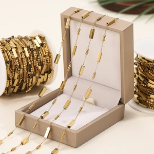 Detailed shot of golden square and bead link chain draped on a beige jewelry box