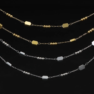 Detail of gold and silver plated stainless steel chains with metallic beads on black background