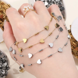 Minimalist heart charm bracelets in gold and silver finish on model's wrist with ring