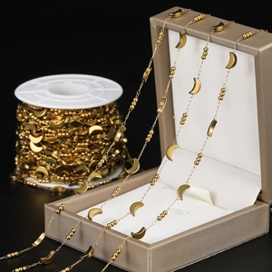 Detail of gold moon and bead link chain draped over a champagne jewelry box