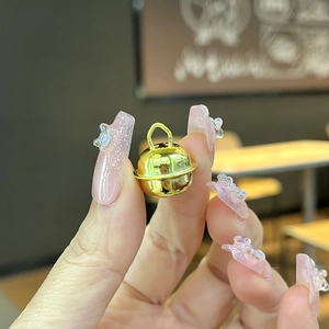 Close-up of a small shiny gold metal bell pendant held in hand for DIY jewelry making