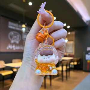 Close-up of cute cartoon girl keychain with orange quicksand details and metal bell charm