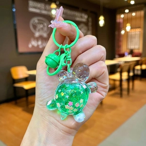 Detail of green turtle quicksand keychain with pink floral sequins and shiny bell