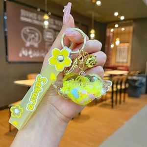 Detail of yellow heart wing keychain with sakura pendant and golden bell on strap