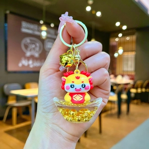 Detail of cartoon dragon keychain with gold bell and transparent ingot base