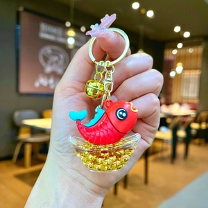 Close-up of a lucky koi fish keychain with red charm and golden bells held in hand