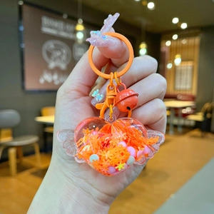 Close-up of orange heart-shaped lollipop keychain with wings and small bell detail