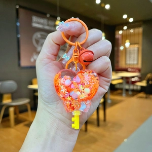 Close-up of heart-shaped orange quicksand keychain with glitters, pearls and small bell