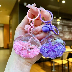 Detailed view of pink and purple acrylic shell liquid glitter keychains held in hand