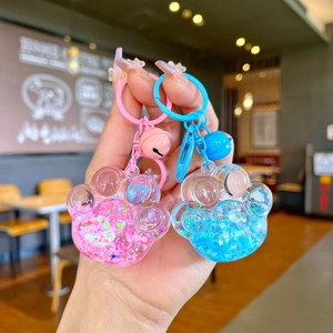 Cute pink and blue cat paw liquid glitter keychains held against a warm cafe background