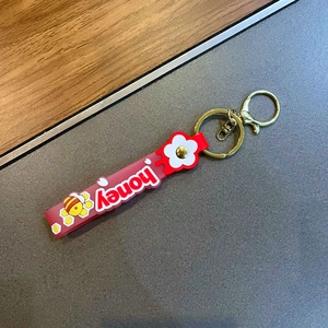Close-up of red PVC honey strap keychain with white flowers and small bee charms
