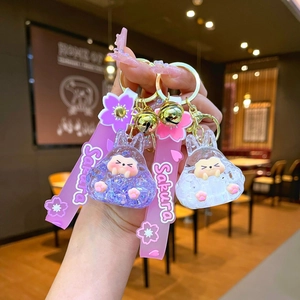 Handheld view of cartoon rabbit keychain with pink Sakura strap and golden bell detail