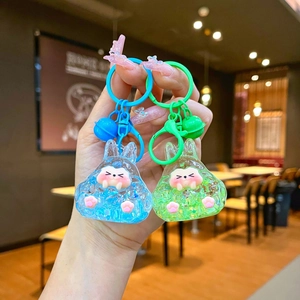 Close-up of blue and green luminous bunny oil liquid sand keychains with matching bells