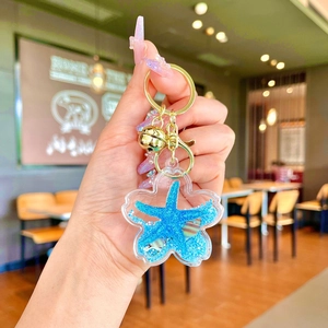 Detail of blue starfish liquid sand flower keychain with golden lobster clasp and bell