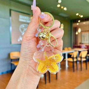 Detail of flower-shaped liquid glitter keychain featuring golden starfish and bell charm
