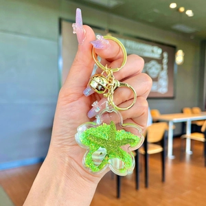 Detailed close-up of a flower-shaped liquid bottle keychain with green glitter and shells