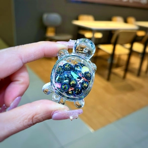 Macro view of a clear resin turtle charm filled with blue glitter balls and sequins