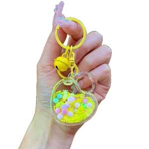 Luminous heart-shaped liquid keychain with yellow beads and sand inside an acrylic bottle