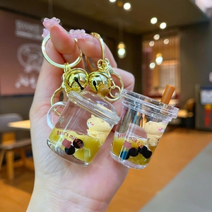 Detailed macro view of two bear bubble tea keychains with liquid sand and a golden bell