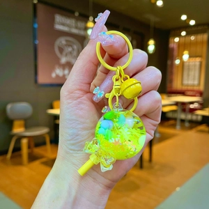 Yellow lollipop keychain with colorful beads and small bell, handheld in warm indoor setting