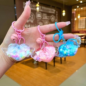 Three colorful winged heart liquid glitter keychains with spring clips in a hand