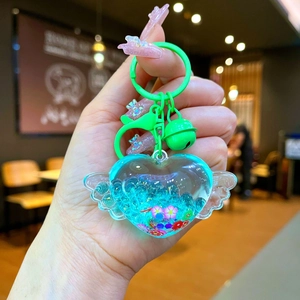 Detail of heart-shaped liquid keychain with wings, sequins, and a green bell accessory