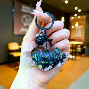 Detail of heart-shaped wing keychain with dark blue shimmering sand and black bell