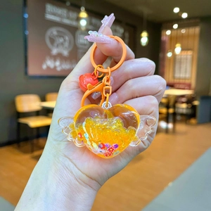 Detailed view of orange heart keychain with glitter, wings, and a small red bell