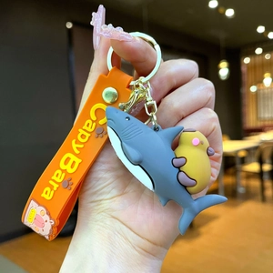 Detail of capybara riding a shark keychain with an orange silicone wristband and gold ring