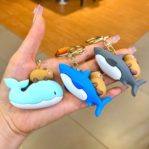Detail of cute Capybara riding blue sharks and whale PVC keychains with gold hooks