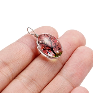 Détail d'un pendentif en verre fait main avec arbre de vie rose tenu entre les doigts