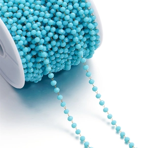 Detail of sky blue faceted crystal beads on a gold-plated stainless steel chain on a spool