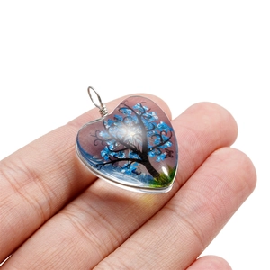 Détail du pendentif en forme de cœur avec arbre de vie bleu tenu dans la main